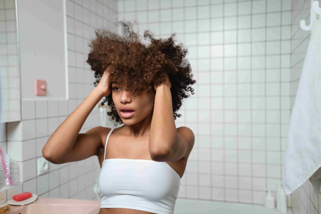 Girl standing in front of mirror thinking about Heat Protectant for Curly Hair